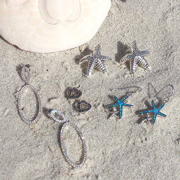 Photo of earrings in sand next to a shell